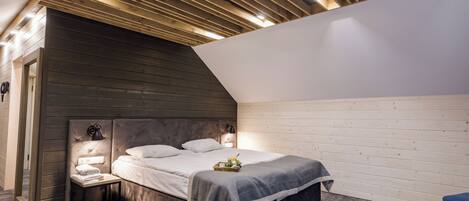 A modern bedroom with a sloped ceiling, a bed with a grey bedspread, bedside lamps, and a small table with a lamp.