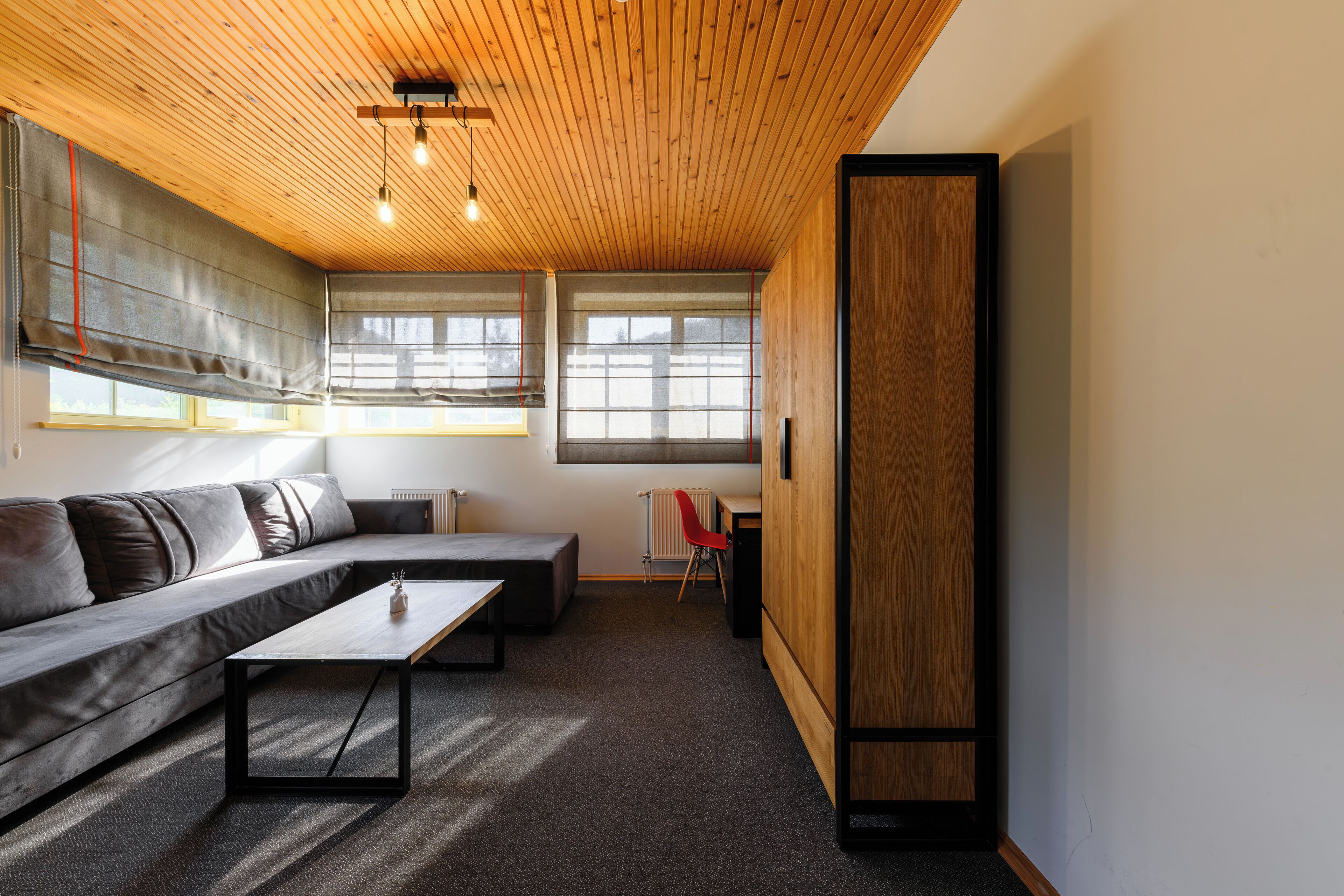 Een moderne woonkamer met een houten plafond, een hoekbank, een salontafel en een rode fauteuil.