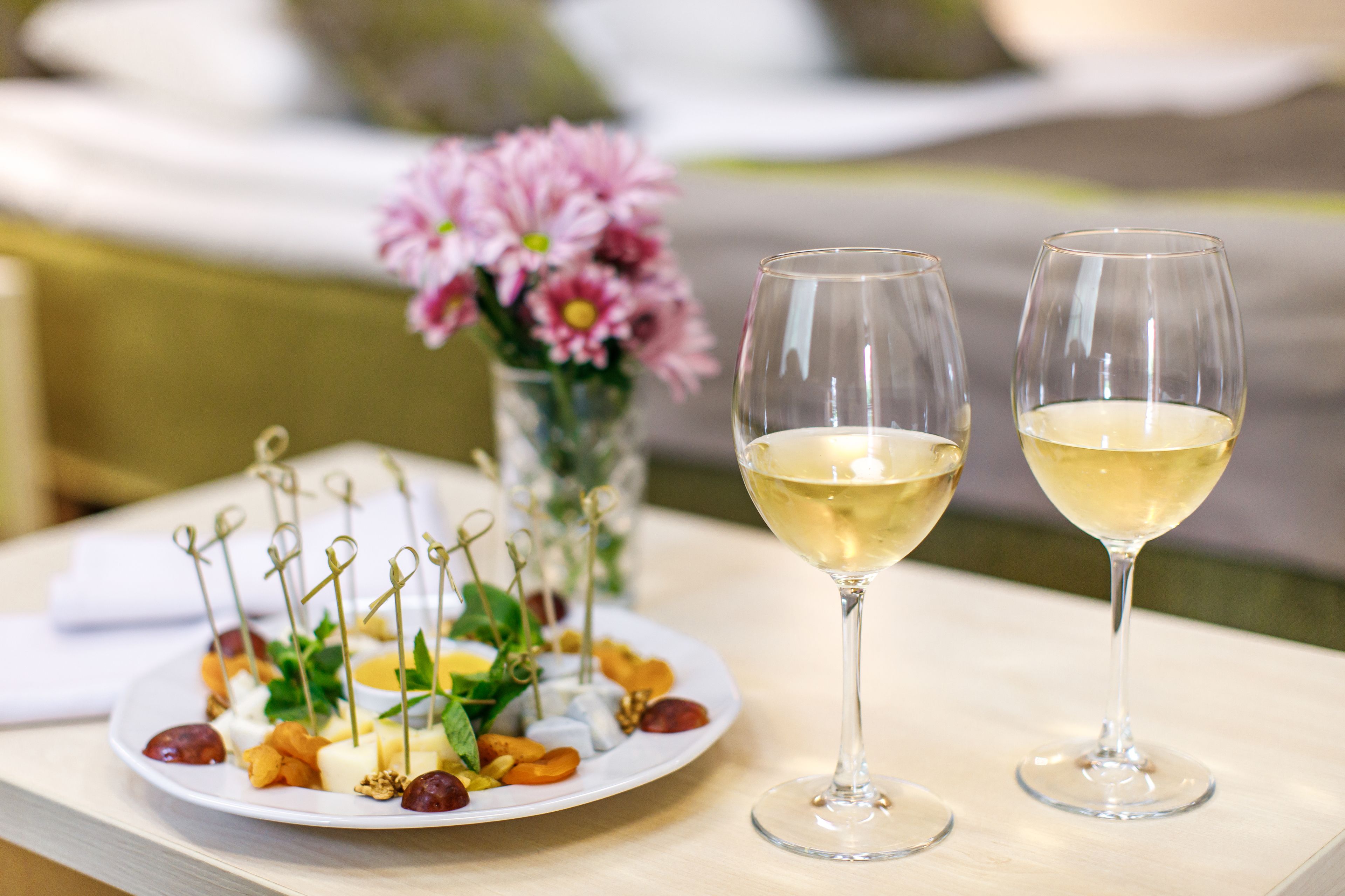 A table with two glasses of white wine and a plate of assorted appetizers.