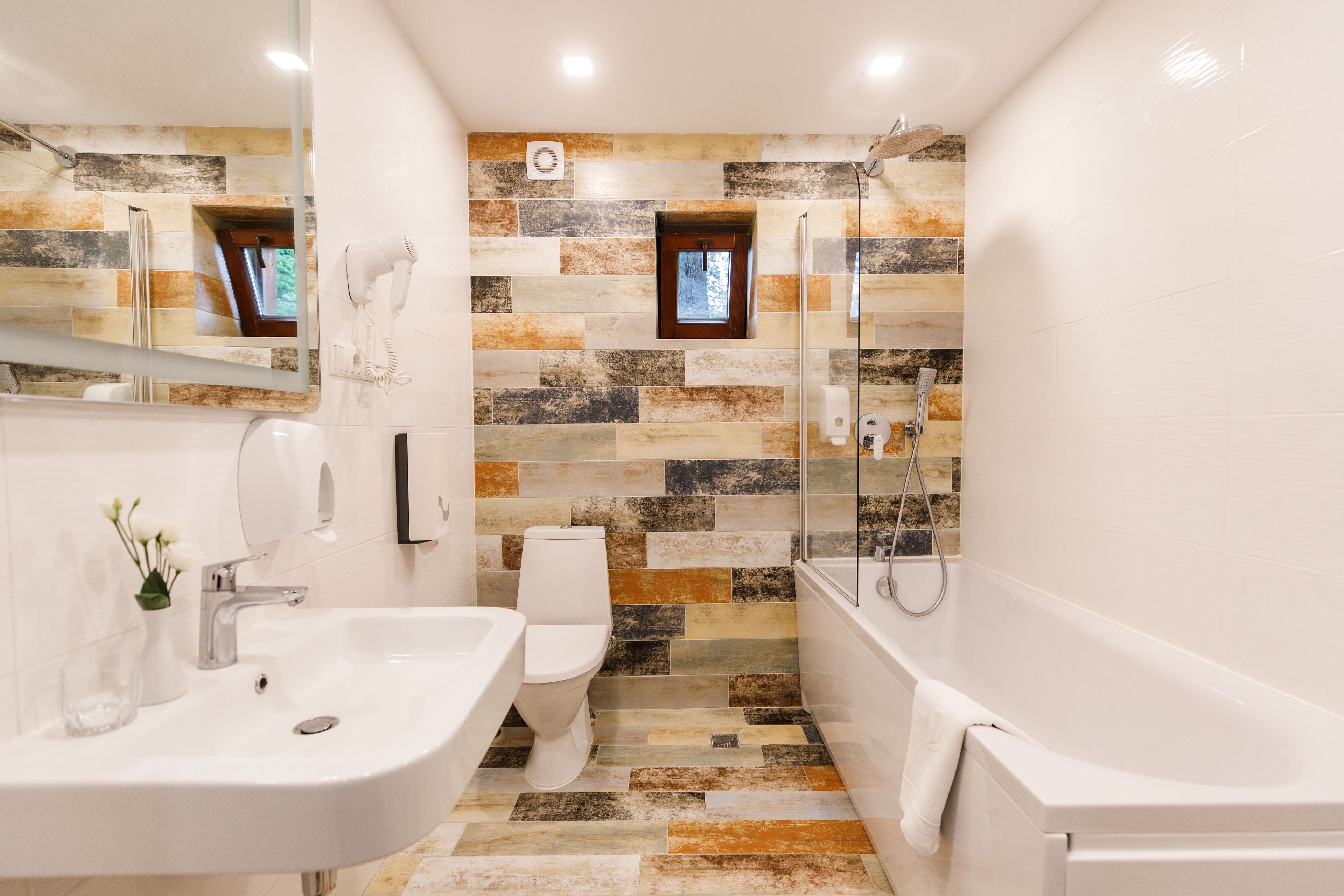 Une salle de bain moderne avec un lavabo, des toilettes et une baignoire blancs, ainsi qu’une douche dotée d’une porte en verre.