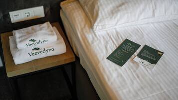 A neatly made bed with white linens and a folded towel on a wooden nightstand. Two informational cards are placed on the bed.