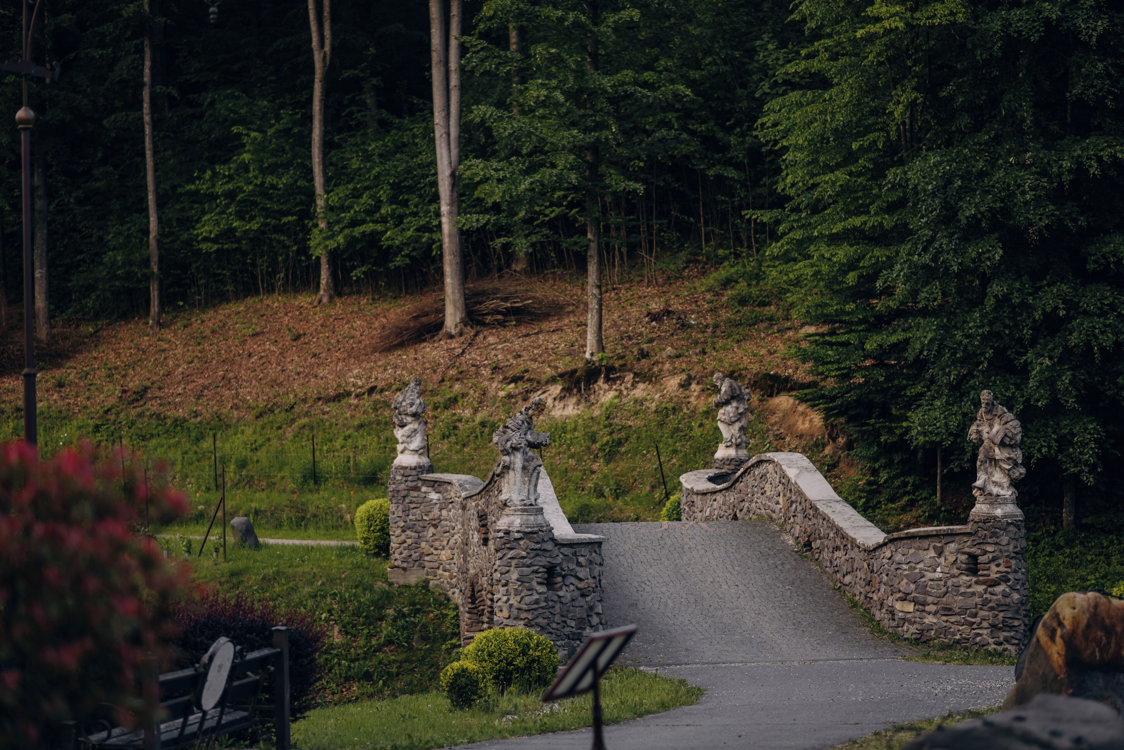 A stone bridge with statues on either side, surrounded by greenery and trees.