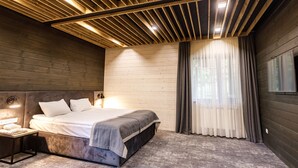 A modern bedroom with a wooden ceiling, a large bed, a nightstand, and a window with curtains. - Voevodyno Resort (Turia Pasika)