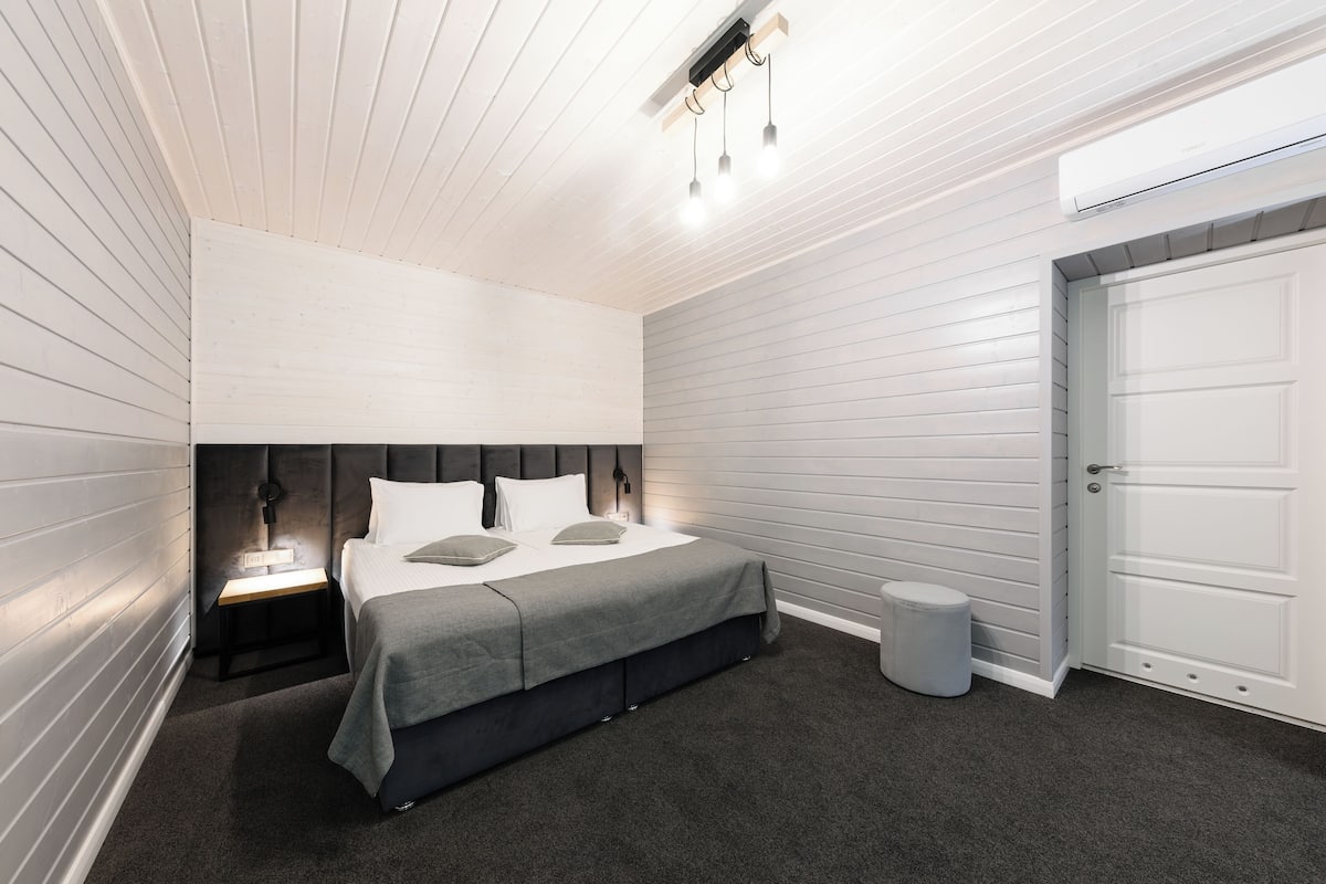 Un dormitorio moderno con cama, mesitas de noche, lámpara de pared y una puerta.