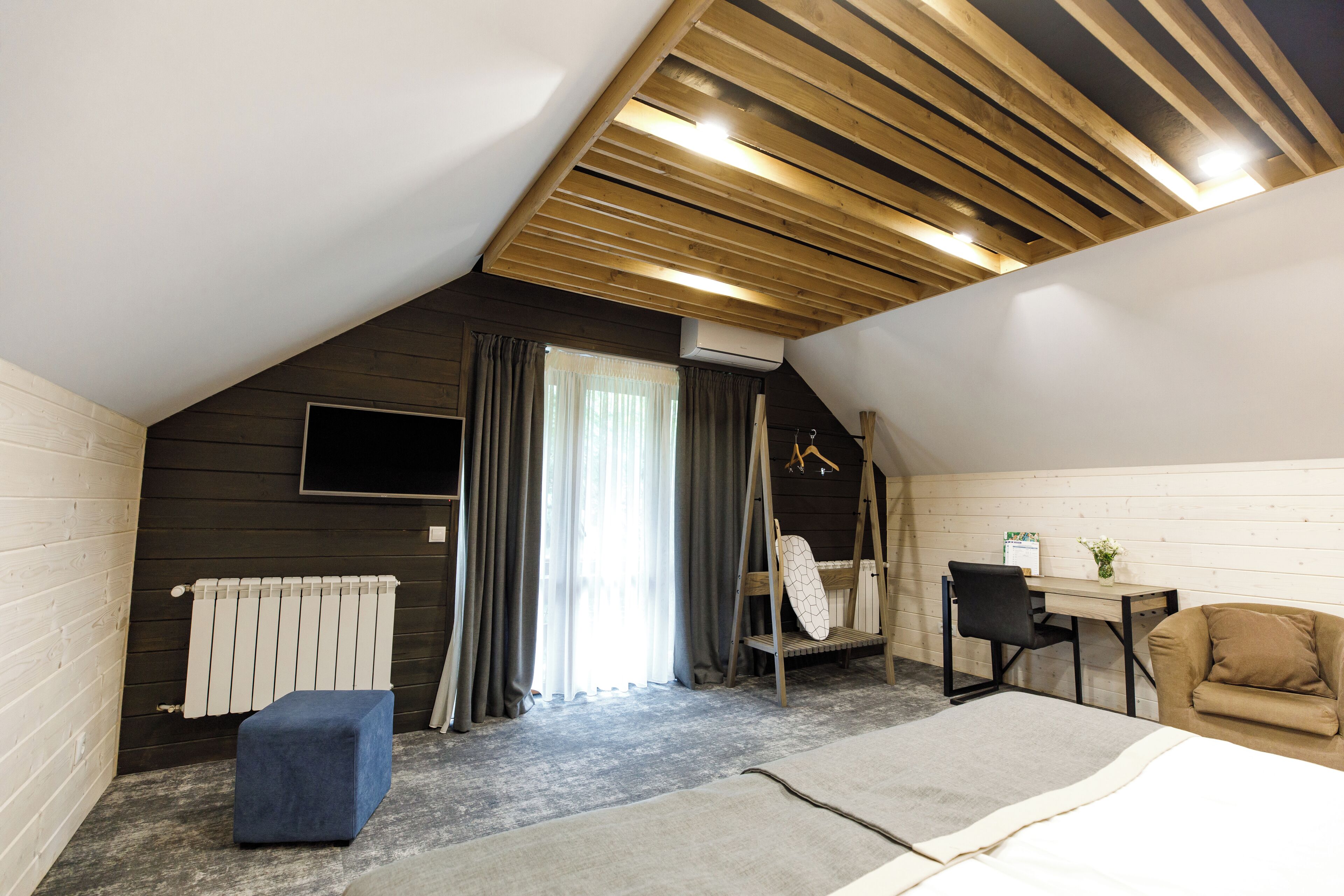 A cozy attic bedroom with a sloped ceiling, a bed, a desk, a chair, and a radiator.