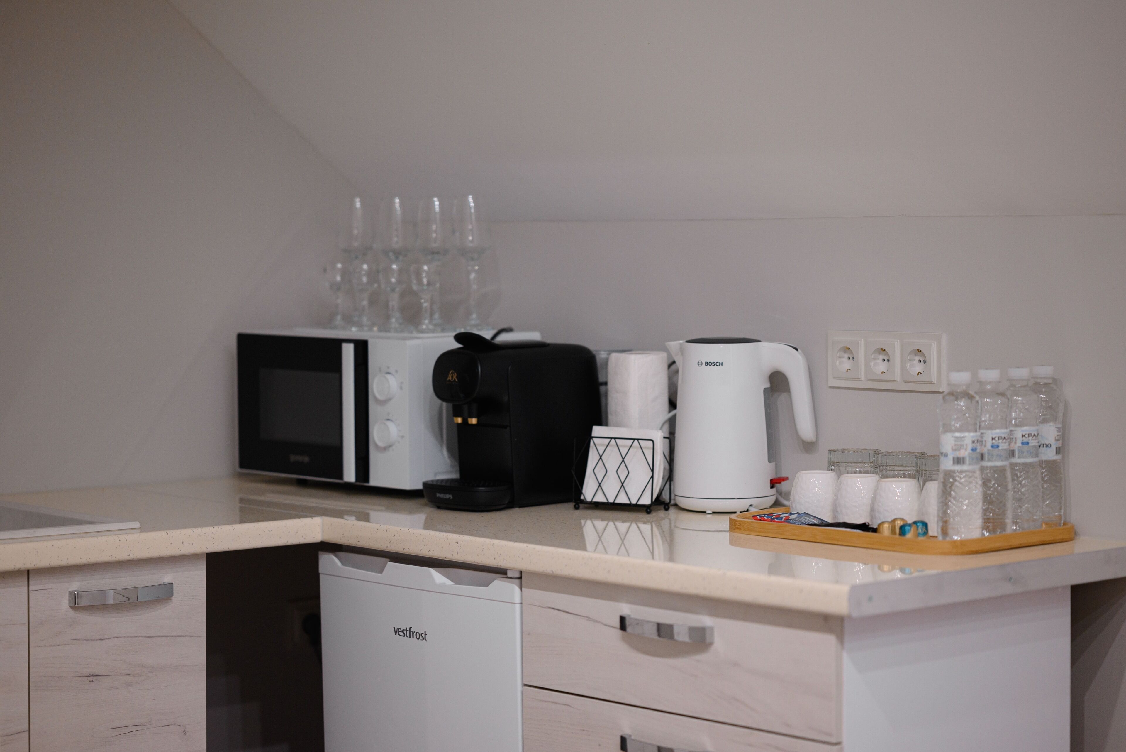 A kitchenette with a microwave, coffee maker, and a coffee pot. There are several glasses and bottles on the counter.