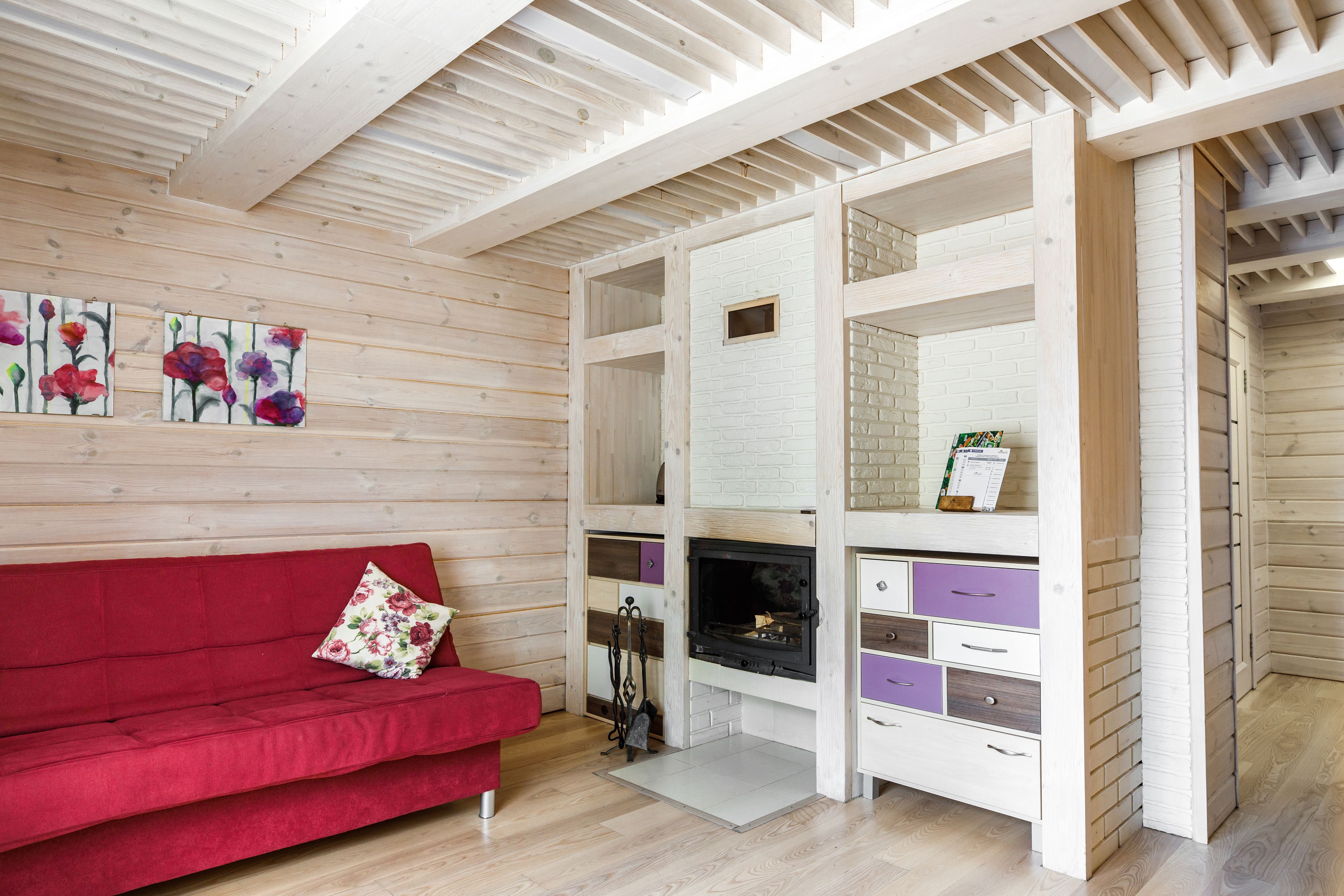 Una habitación con sofá rojo, paredes de madera, chimenea y pared decorativa de ladrillo blanco.