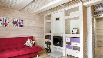 Una habitación con sofá rojo, paredes de madera, chimenea y pared decorativa de ladrillo blanco.