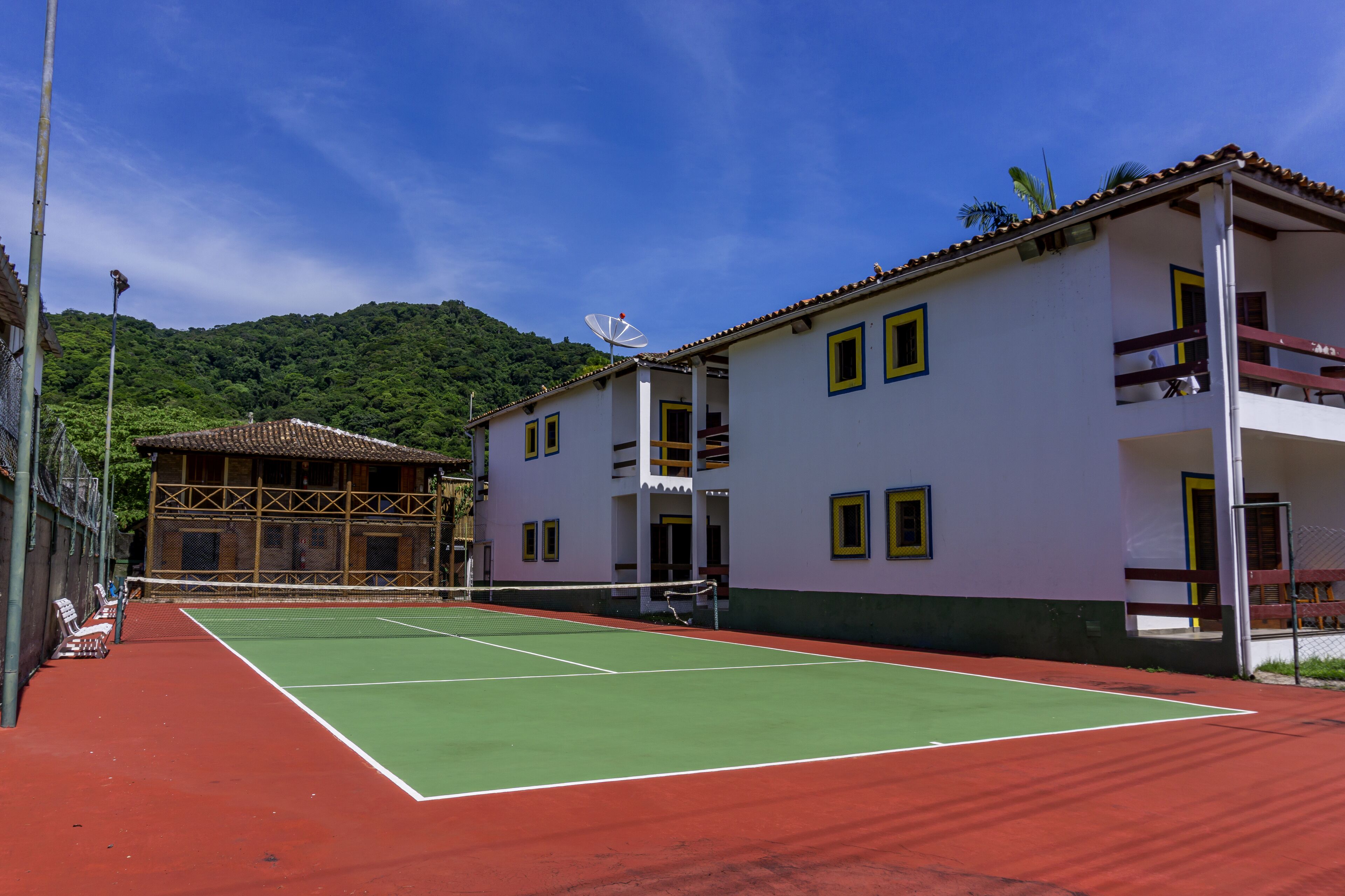 A tennis court with a net, surrounded by buildings with balconies and a mountain in the background.