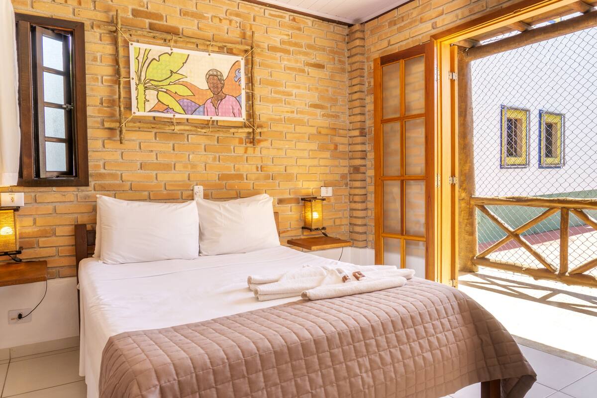 A hotel room with a brick wall, a bed with white bedding, two bedside lamps, and a view through a wooden door.