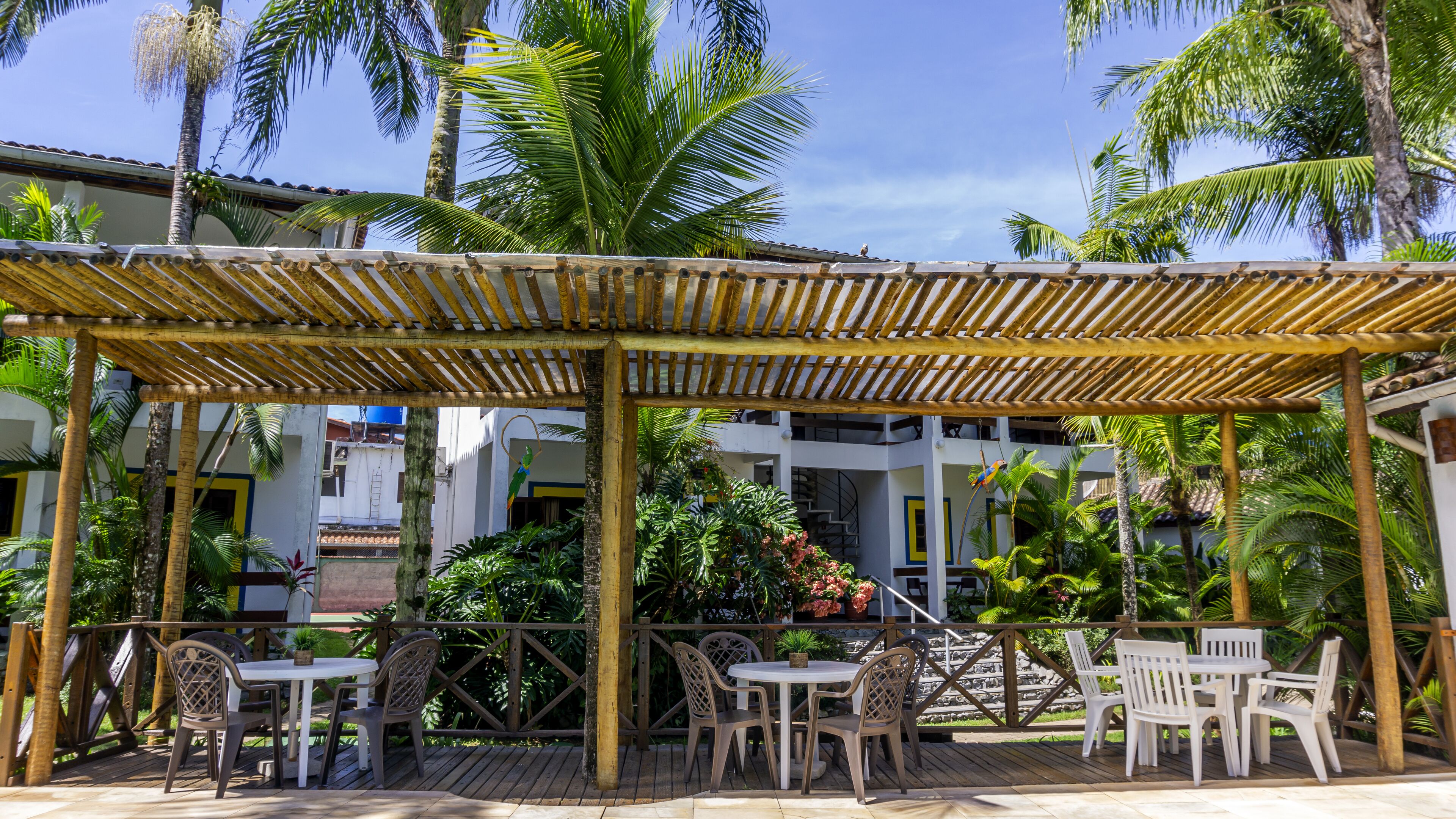 An outdoor patio with bamboo pergola, white and brown chairs, and tables.