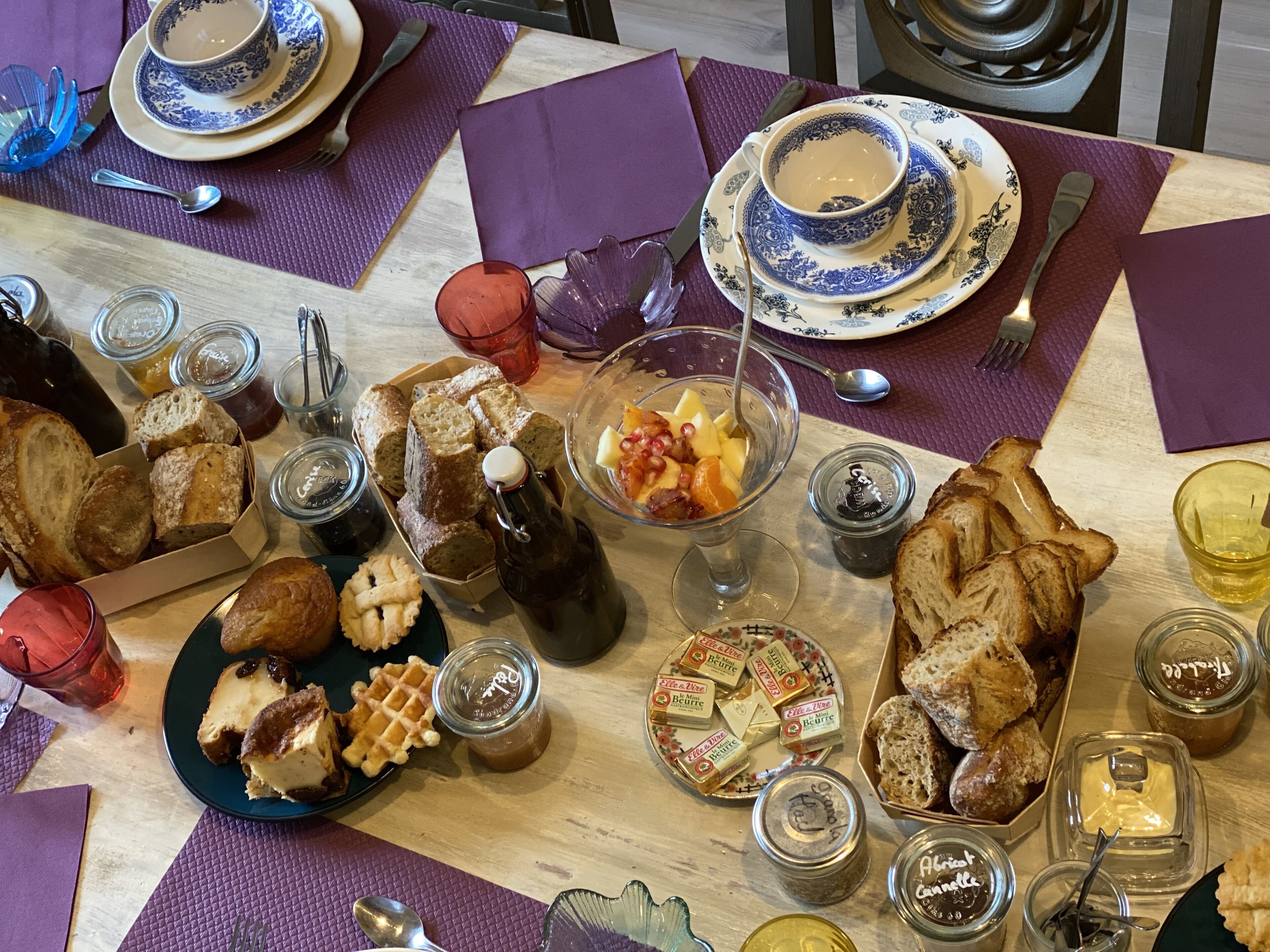 Una mesa servida con diversos alimentos, como pan, gofres y un bol de fruta.
