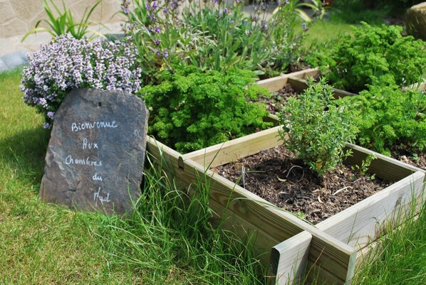 A garden with raised wooden planters containing various plants and a stone with 'Bienvenue' written on it. - Les Chambres du Mad (Henvic)