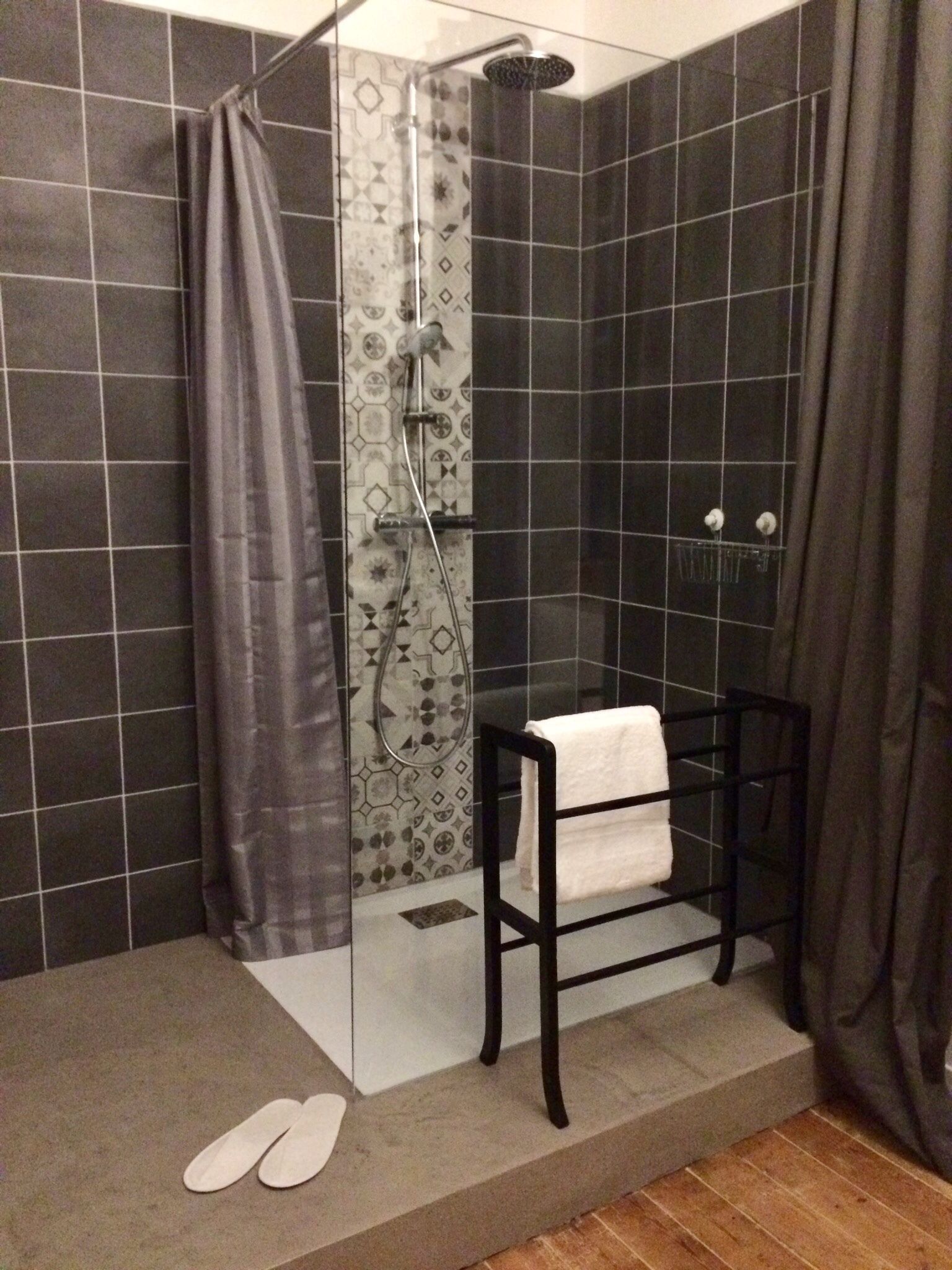 Un área de ducha con puerta de cristal, un perchero y un par de zapatillas en el suelo.