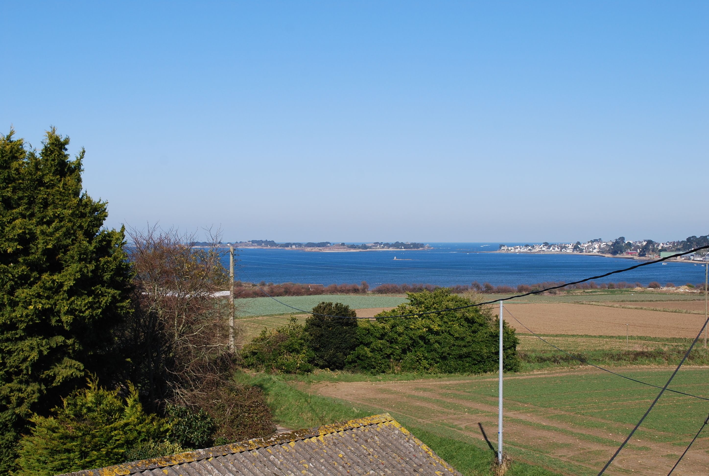 Un paisaje costero con vista al mar, cielo despejado y un pueblo lejano.