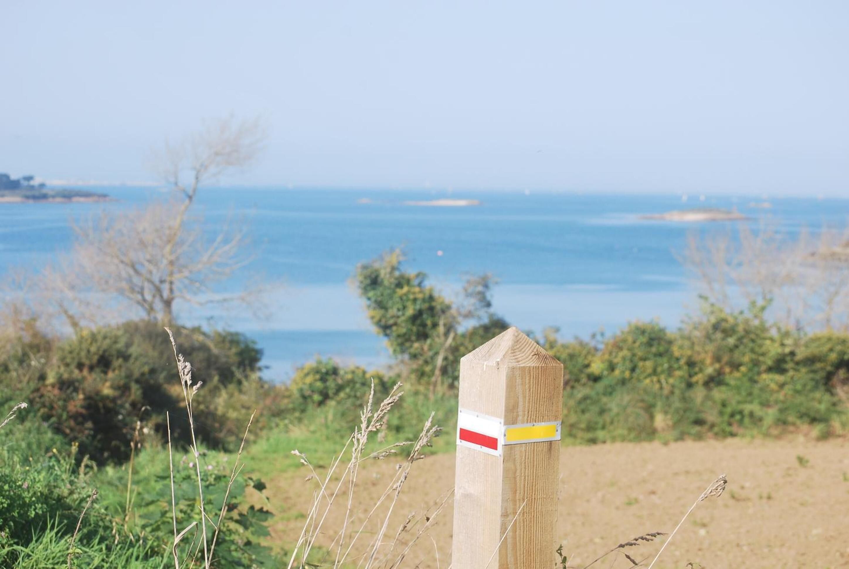 A wooden post with a white and red stripe, set against a coastal landscape with a clear view of the sea and distant land.