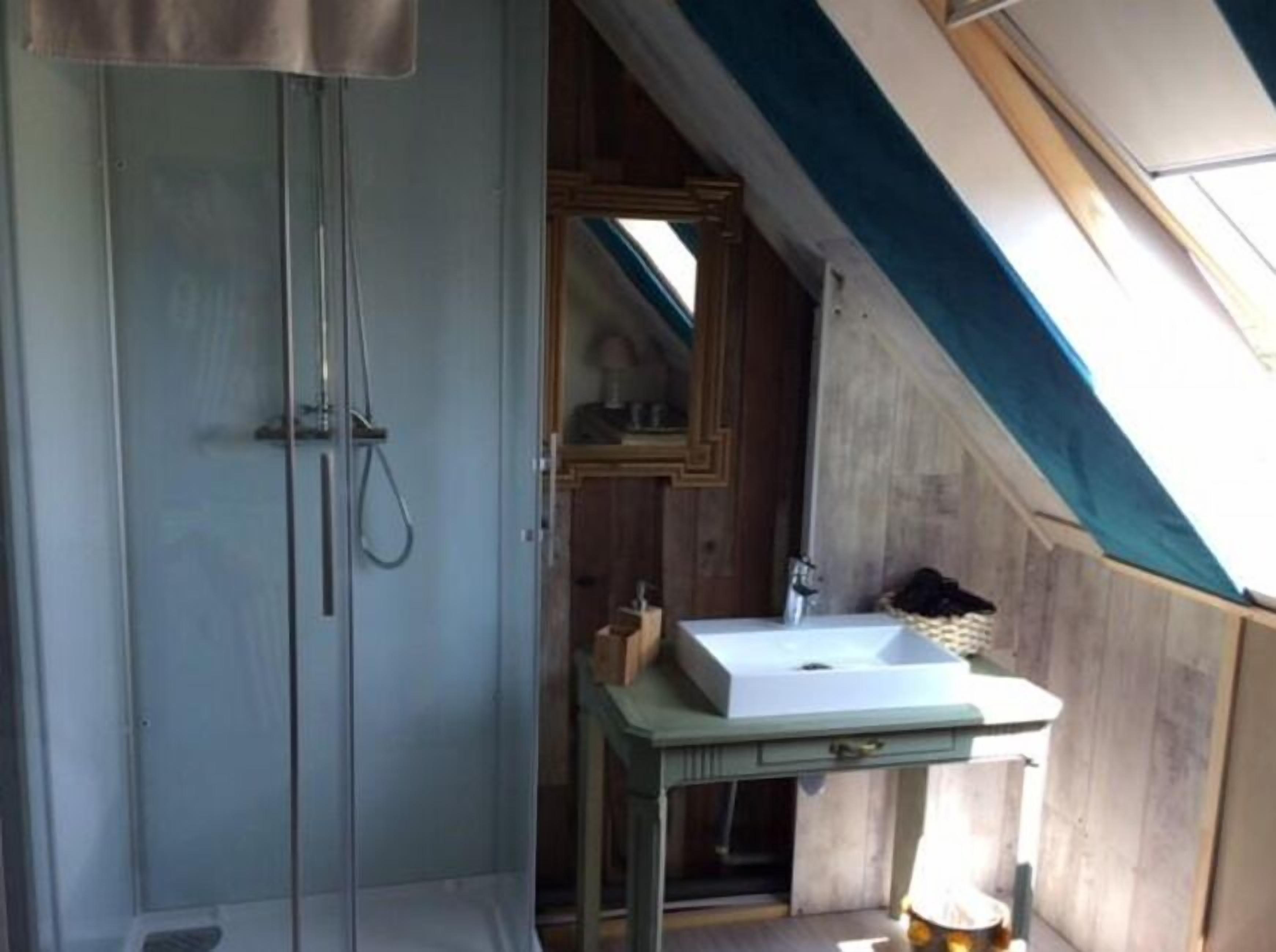 Una piccola camera da letto in mansarda, con una finestra a lucernario, un armadio in legno e un semplice comodino con lavandino.