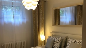 Hotellihuone, jossa on sänky, patteri, ikkuna verhoilla, seinälle kiinnitetty peili ja kattovalaisin.