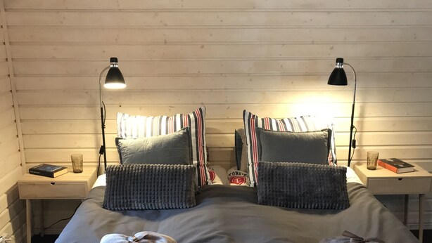 Una cama con dos camas individuales, almohadas a rayas, una mesita de noche con una lámpara y una pequeña mesa con un libro y un vaso.