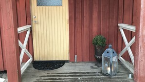 Una puerta de madera con felpudo, planta en maceta y farol en el porche.
