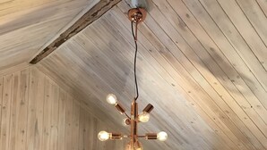 Techo de madera rústico con vigas a la vista y una lámpara colgante central con varias bombillas.