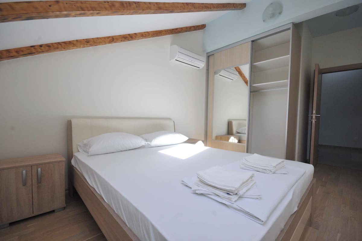 A bedroom with a bed, a nightstand, a wardrobe, and an air conditioning unit.