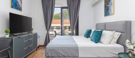 Habitación de hotel moderna con una cama grande, una televisión de pantalla plana, un escritorio y un balcón con vista a un edificio.