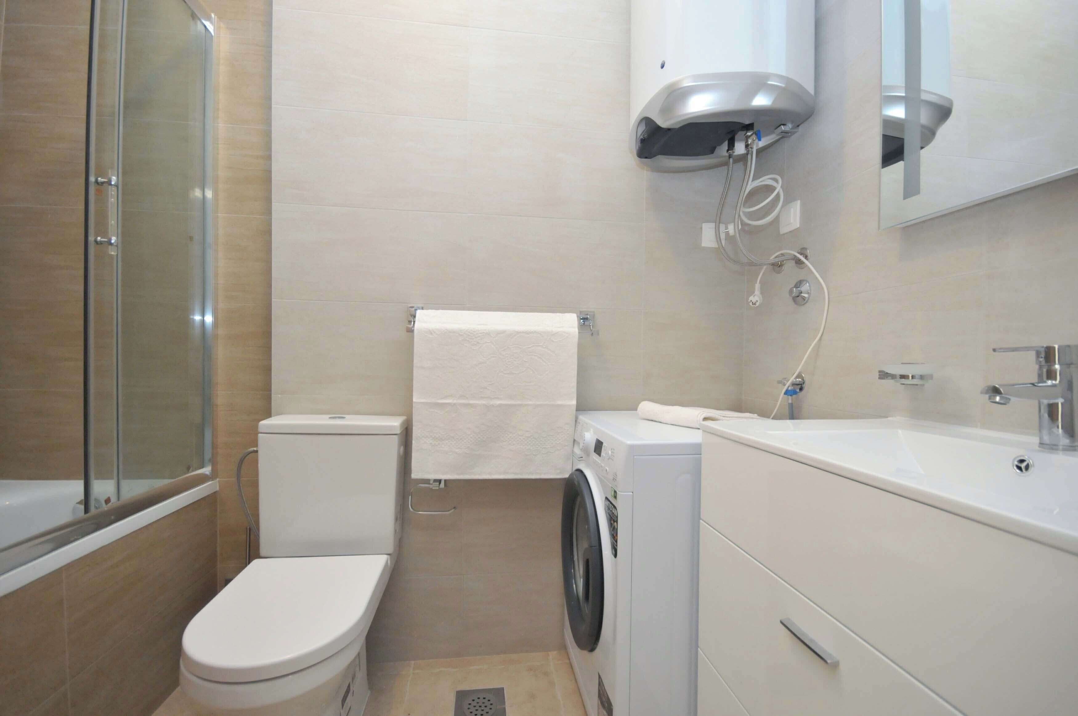 A compact bathroom with a toilet, washing machine, and sink.