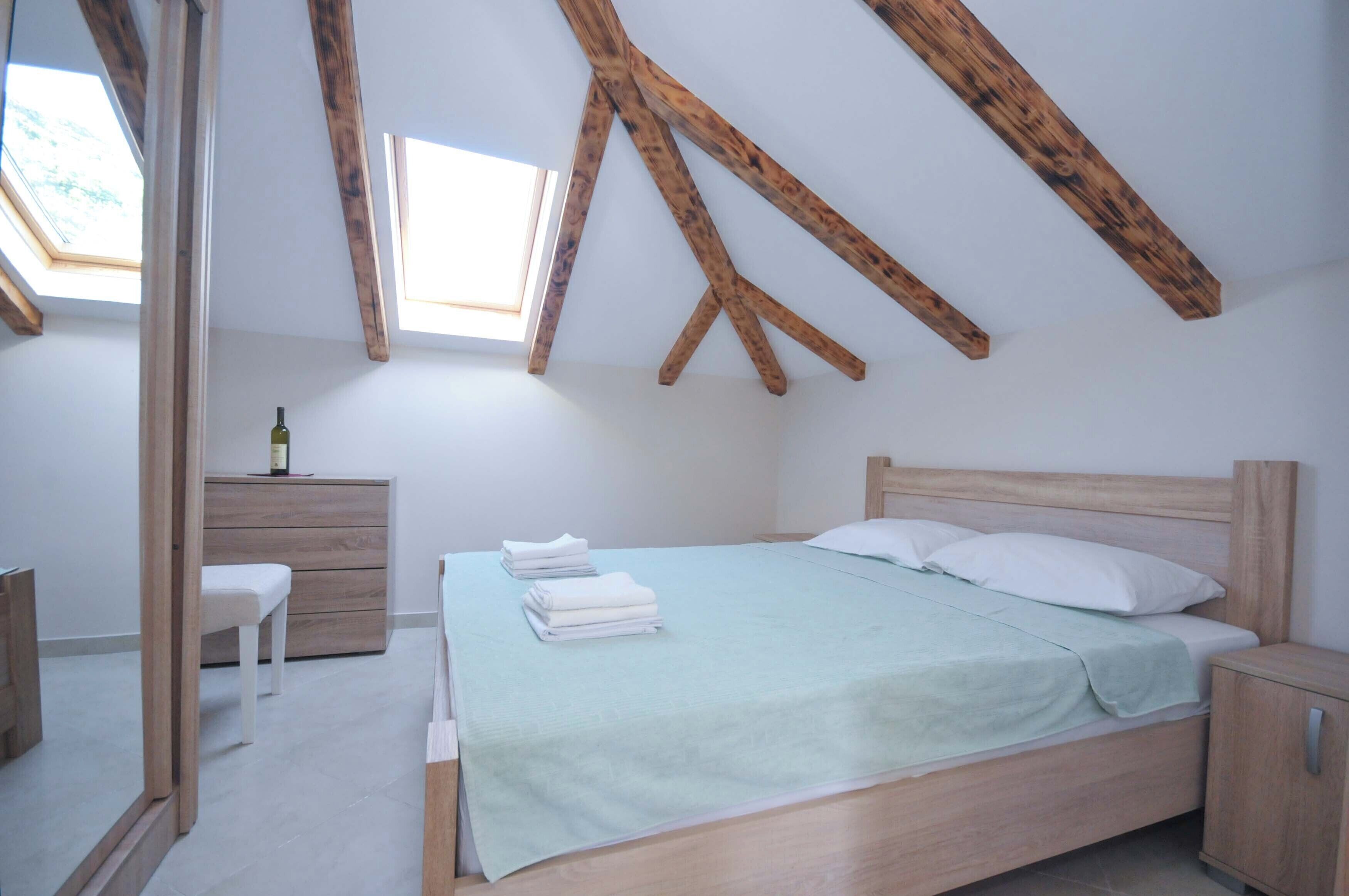 A bedroom with a wooden ceiling, a bed with a green bedspread, a bedside table, a chair, and a small cabinet.