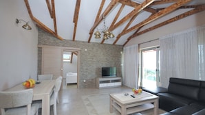 Una sala de estar moderna con techo de madera, un televisor sobre un mueble, una mesa de comedor con sillas y un sofá negro.