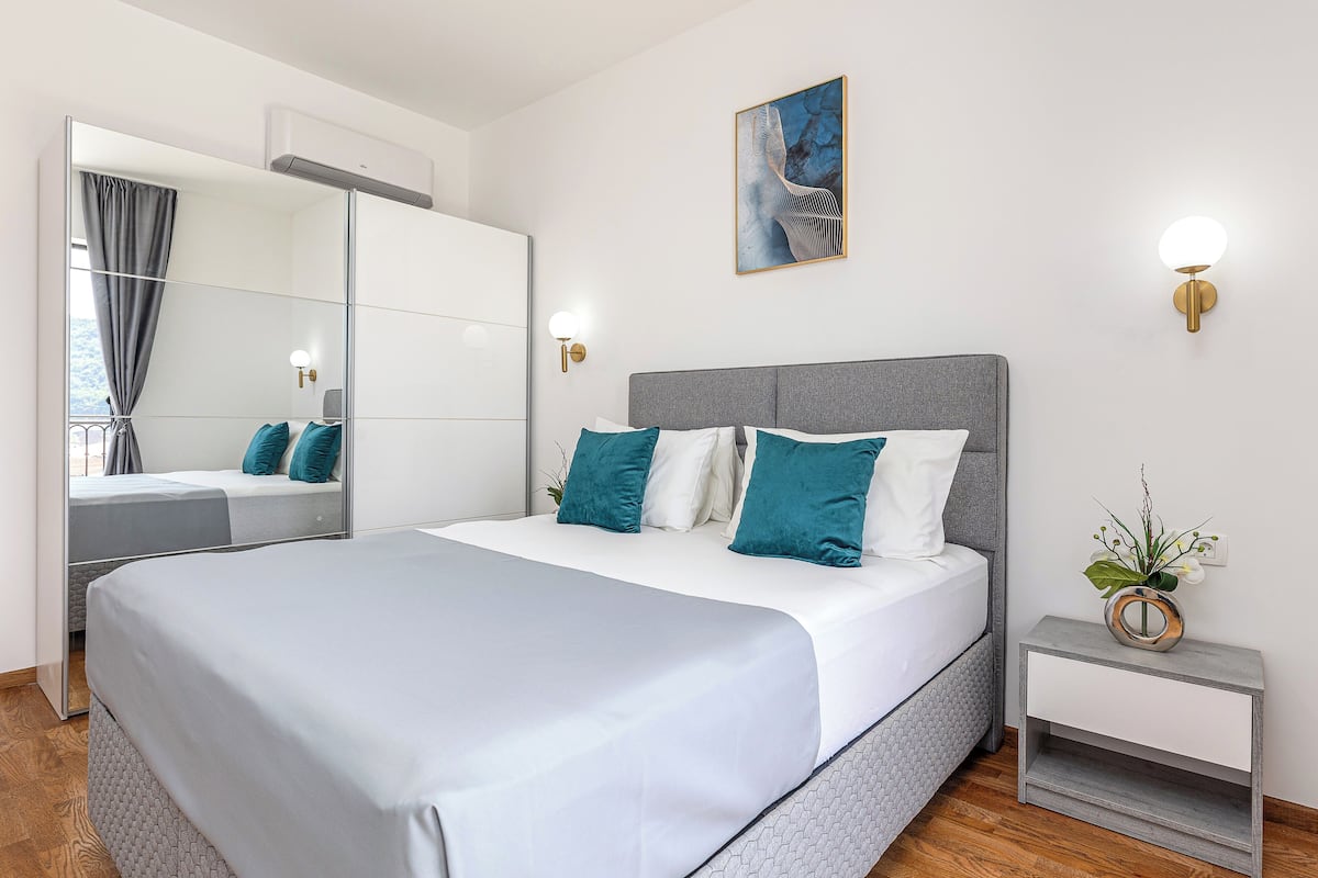 A modern bedroom with a large bed, a bedside table, a wall-mounted light, and a mirror.