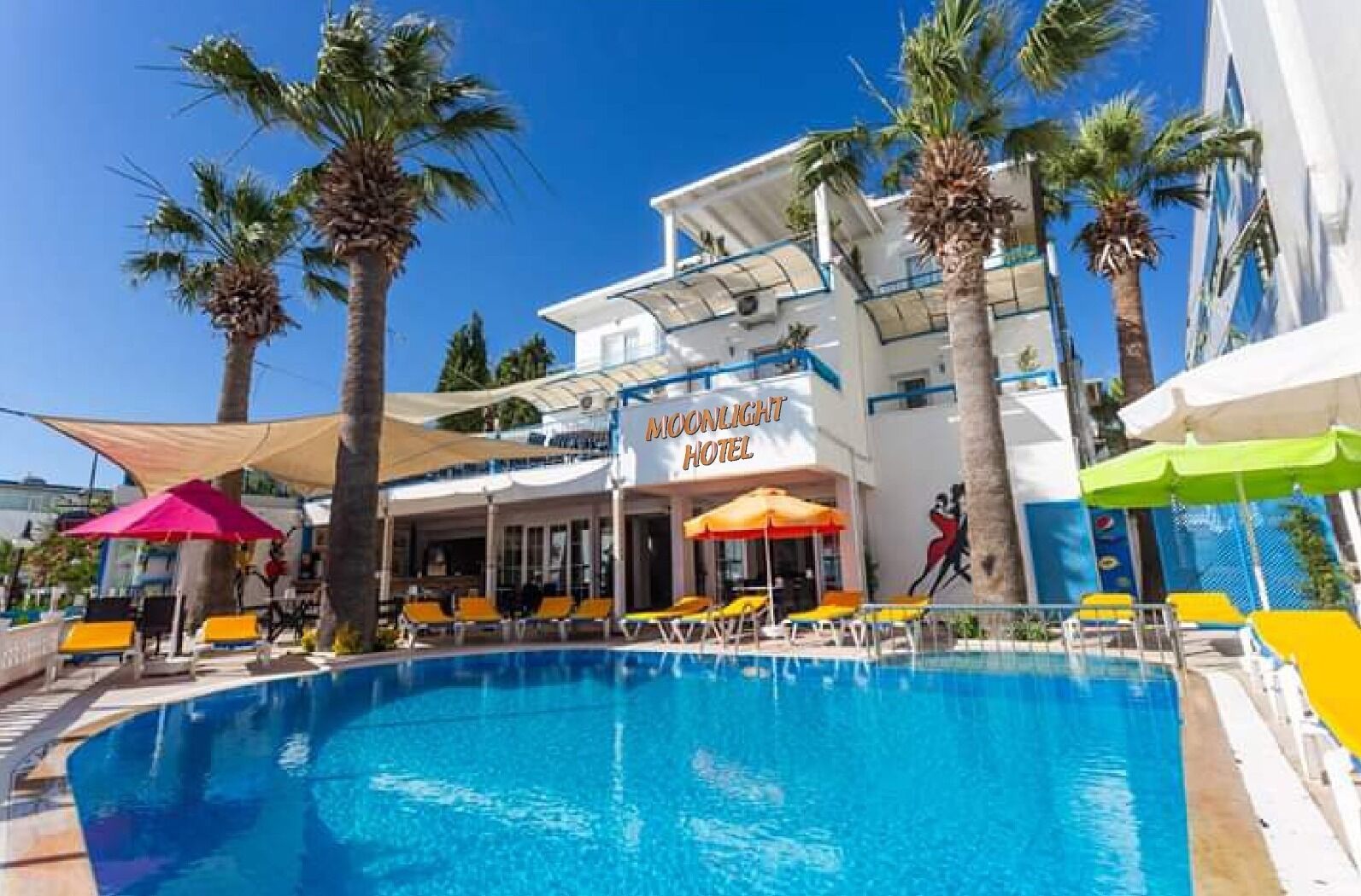 A hotel with a pool, palm trees, and outdoor seating.