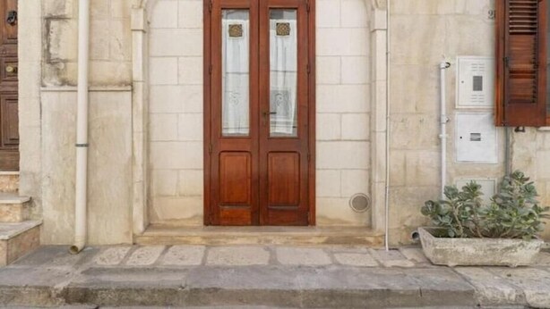 Une entrée d’immeuble avec une porte double en bois, un mur en pierre et un pot de fleurs placé sur la droite.