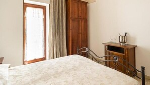 Une chambre à coucher comprenant un lit, une armoire en bois, une chaise à ossature métallique et une petite table sur laquelle se trouve une carafe.