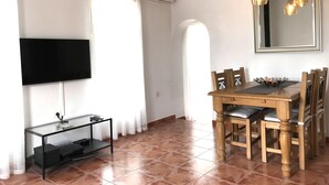 A dining area with a wooden table and chairs, a glass TV stand, and a wall-mounted clock. - Villa Estrella with private pool and hottub in Mazarron (Mazarrón)