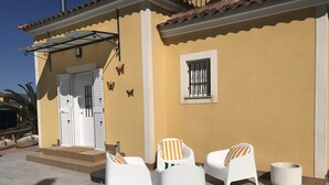 A yellow building with a white door, a window with bars, and two white chairs with striped cushions. - Villa Estrella with private pool and hottub in Mazarron (Mazarrón)