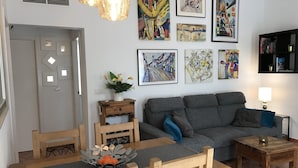 A modern living room with a grey sofa, wooden dining table, and chairs. There are several framed artworks on the wall, a small side table with a lamp, and a decorative bowl on the table. - Villa Estrella with private pool and hottub in Mazarron (Mazarrón)