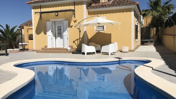 A poolside area with a swimming pool, white outdoor furniture, and a building with a tiled roof. - Villa Estrella with private pool and hottub in Mazarron (Mazarrón)