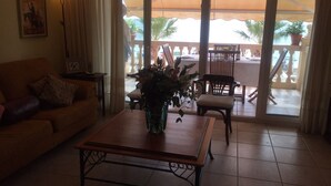 A living room with a sofa, a coffee table with a vase, and a view of an outdoor balcony with chairs and potted plants. - Beautiful apartment facing the sea with huge terrace (El Campello)