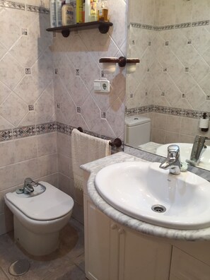 Une salle de bain avec des toilettes, un lavabo et un miroir. Une serviette est accrochée au mur et une étagère contient des articles de toilette.