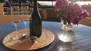 Ein Tisch mit einer Flasche, Gläsern und einer Blumenvase auf einem Balkon mit Blick auf Gebäude.