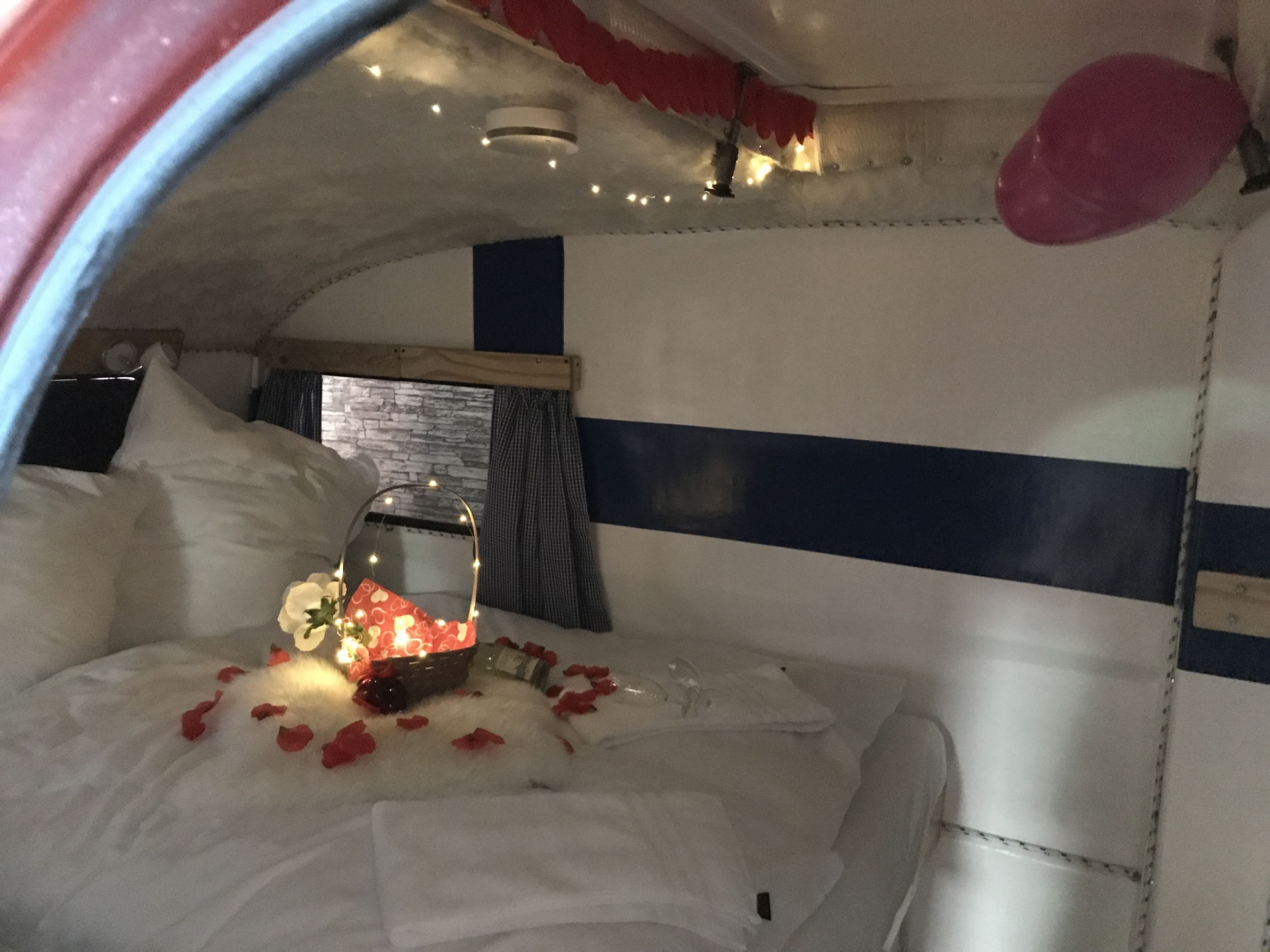 Ein gemütliches Bett mit weißer Bettwäsche, ein Blumenkorb und Rosenblätter, die verstreut liegen.