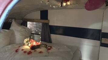 Ein gemütliches Bett mit weißer Bettwäsche, ein Blumenkorb und Rosenblätter, die verstreut liegen.