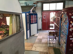 Un couloir étroit doté d’un plancher en bois, d’une porte rouge et d’un mur recouvert d’autocollants.