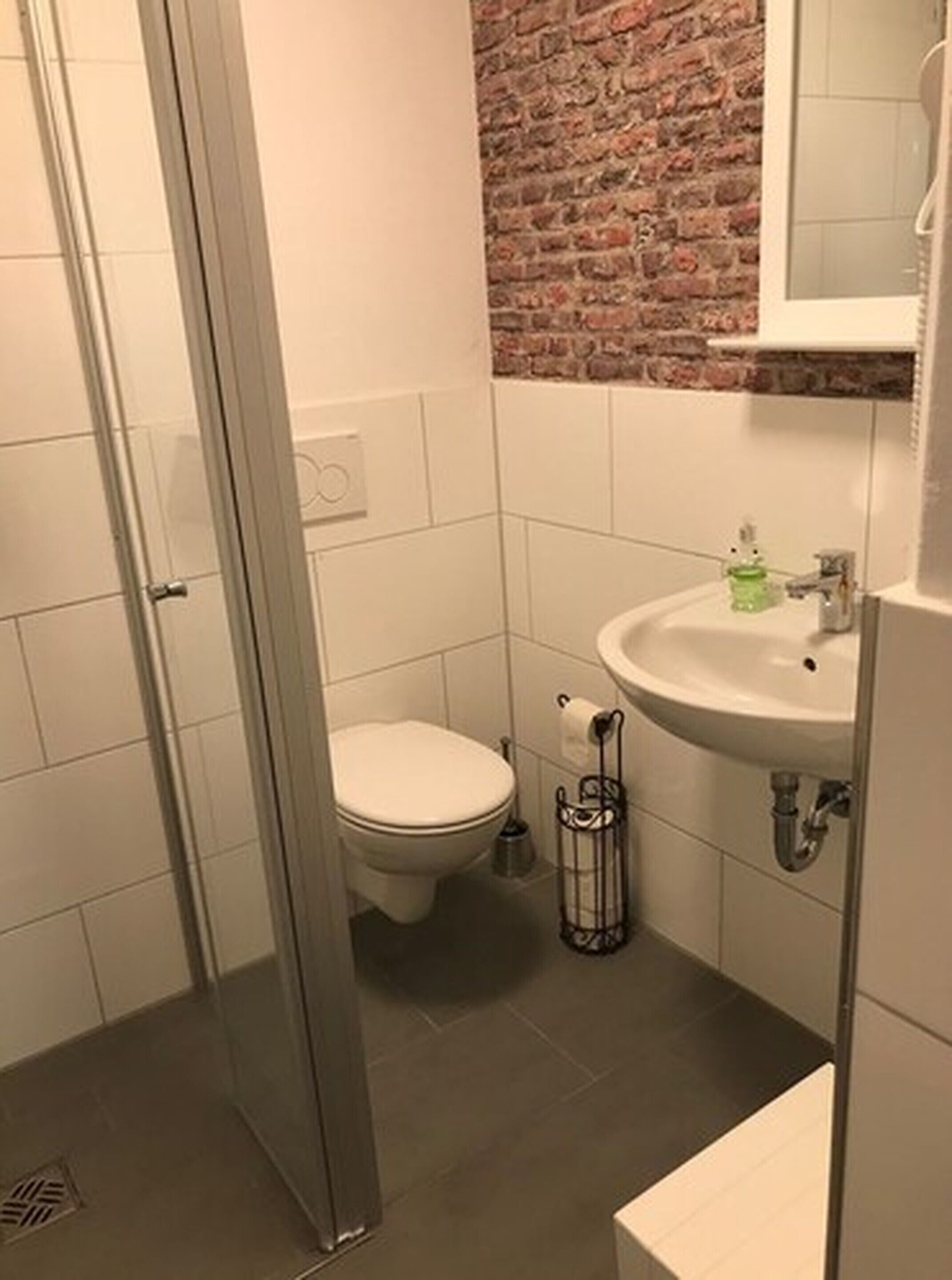 Un baño con mampara de vidrio, inodoro y lavamanos con espejo.