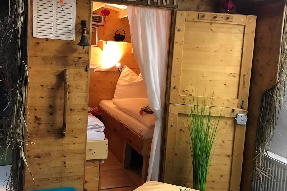 A wooden hut with a sign reading "VIETNAM". Inside, there is a bed, a small table with a plant, and a blue bench.