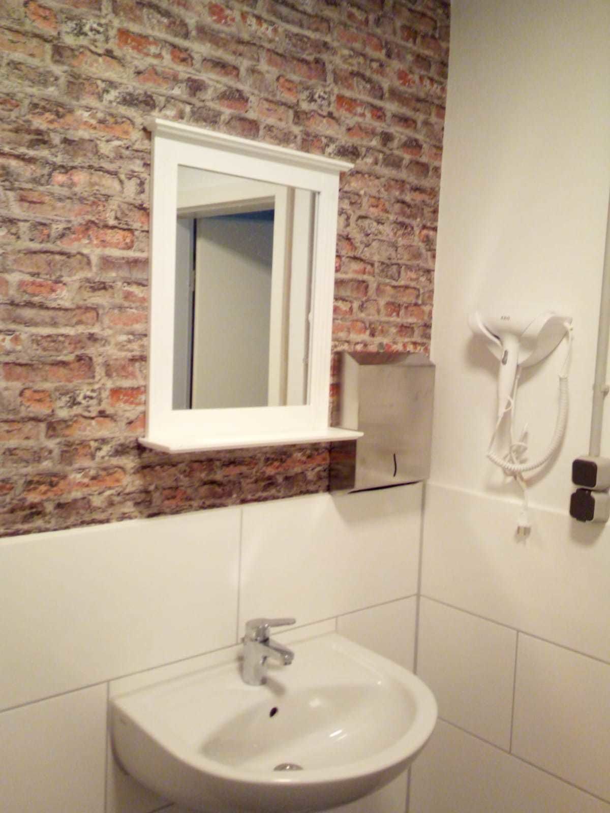 Un baño con un lavabo blanco, un espejo y un secador de pelo montado en la pared.