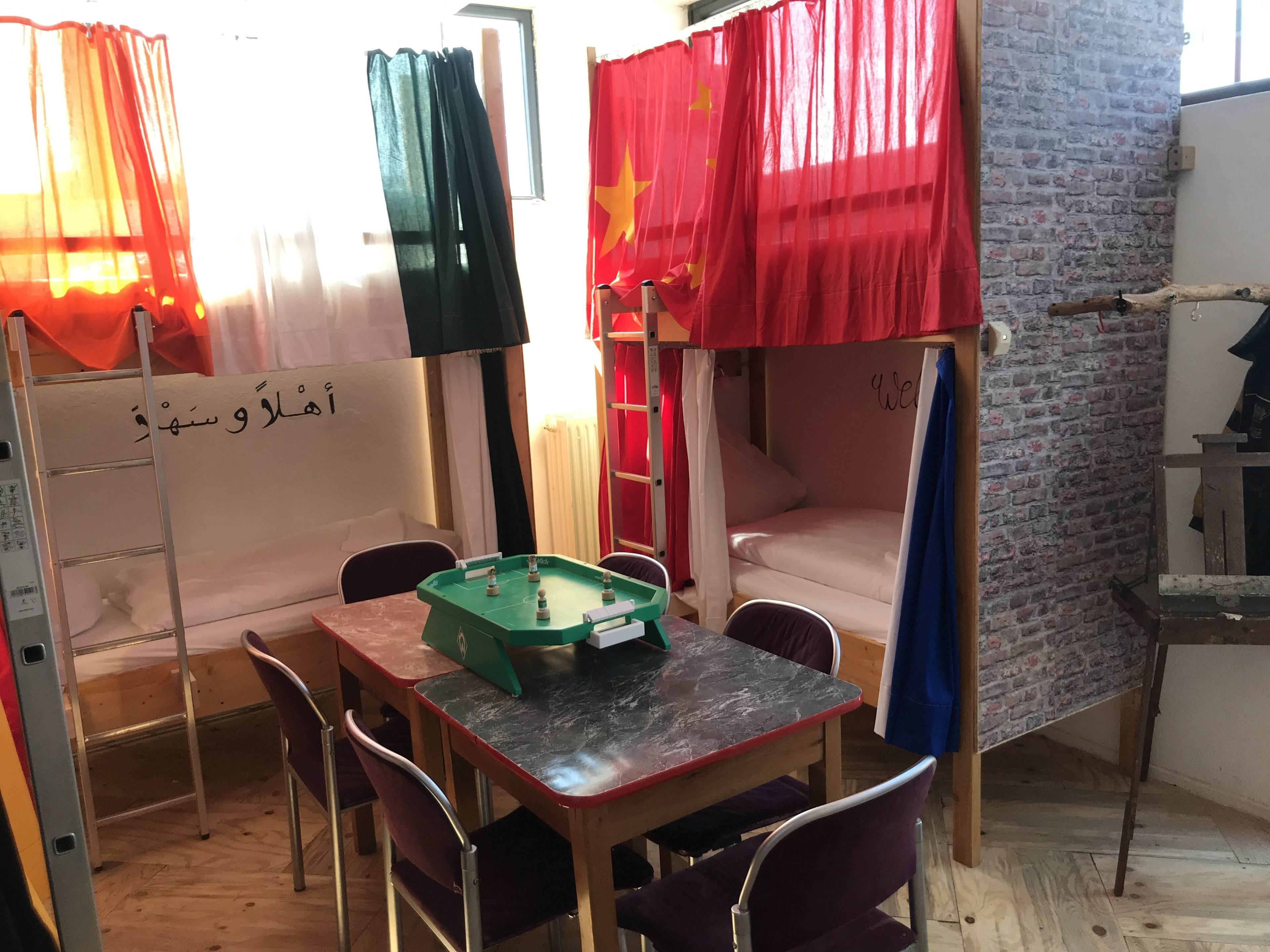 A room with bunk beds, a table with a foosball table, and a whiteboard with text.