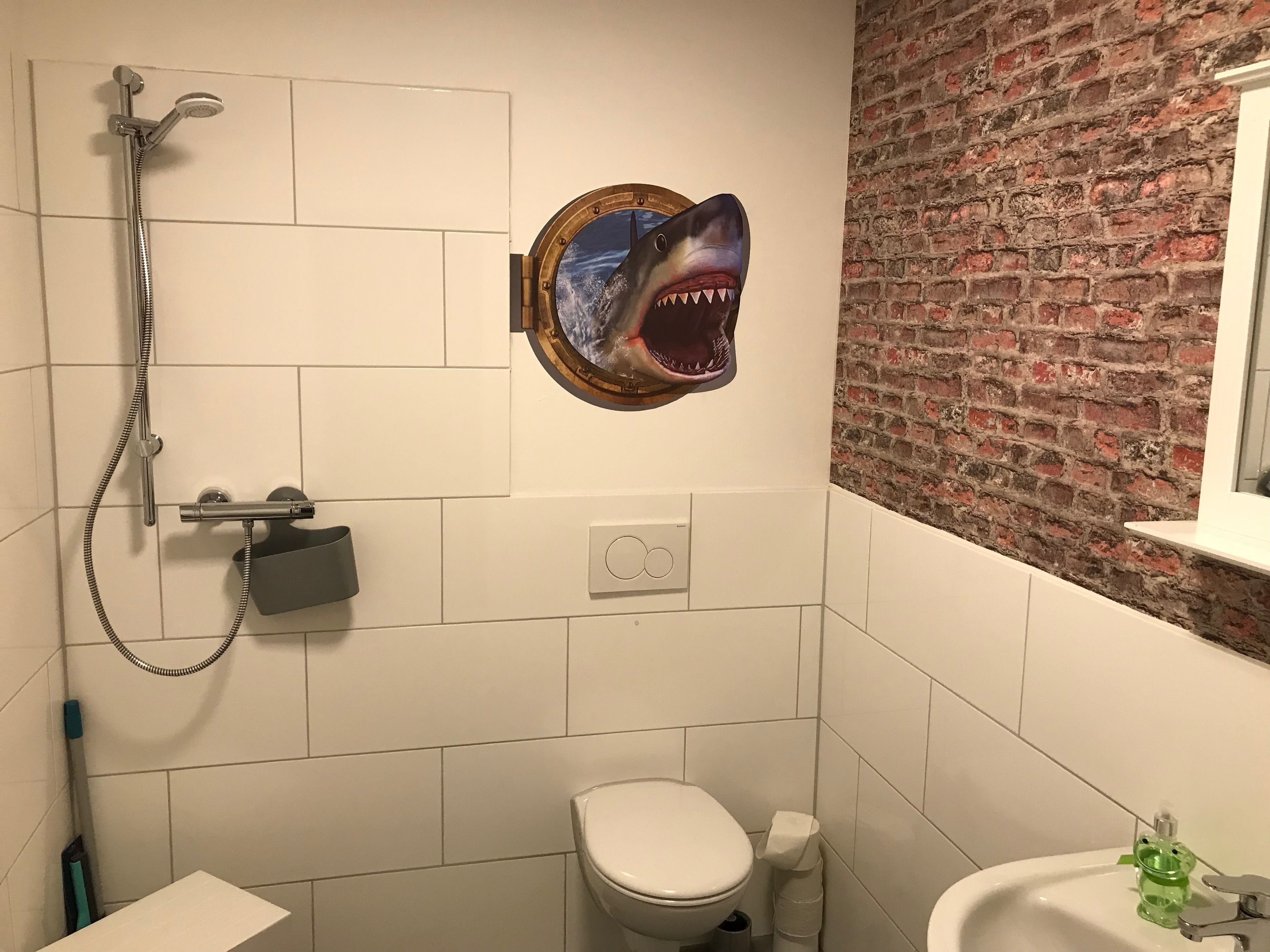 Ein Badezimmer mit Dusche, Toilette, Waschbecken und einer Wanddekoration zum Thema Hai.