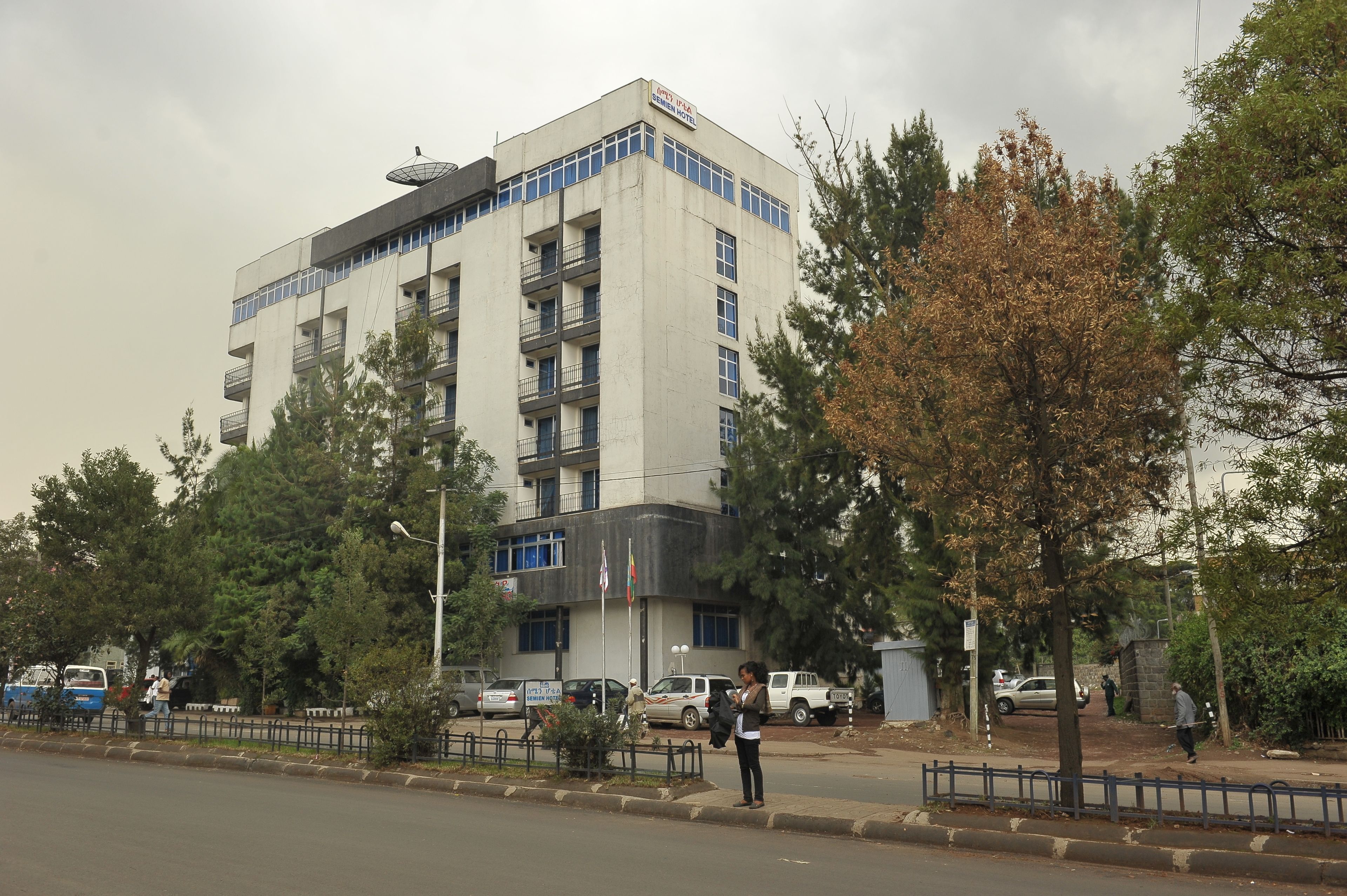Un edificio de varios pisos con balcones, una señal que indica que es un hotel y un asta con banderas.